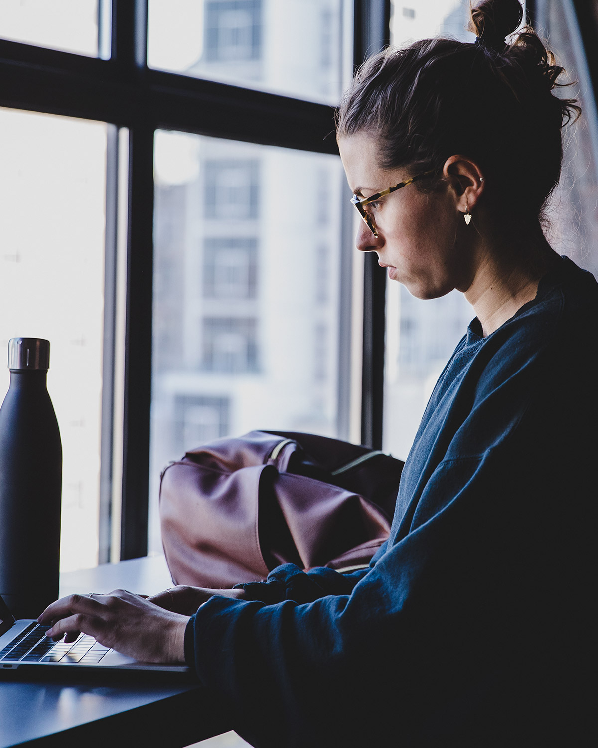 Student working on laptop at window in common area