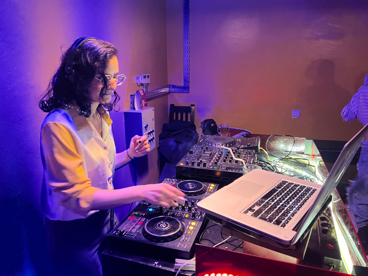 Female DJ shown with a deck and laptop in a music studio.
